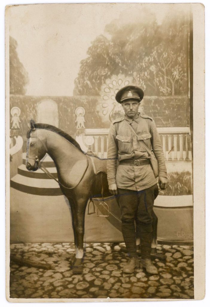 Soldier posing with fake horse in front of painted backdrop.